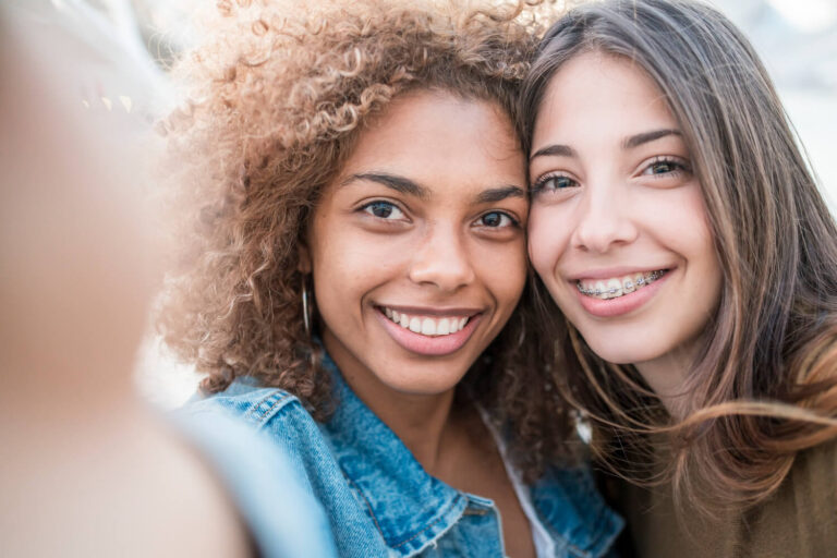 Duas jovens sorridentes em Higienópolis, uma usando aparelho fixo metálico e outra com sorriso livre, discutindo alinhadores invisíveis na Gen Odontologia.